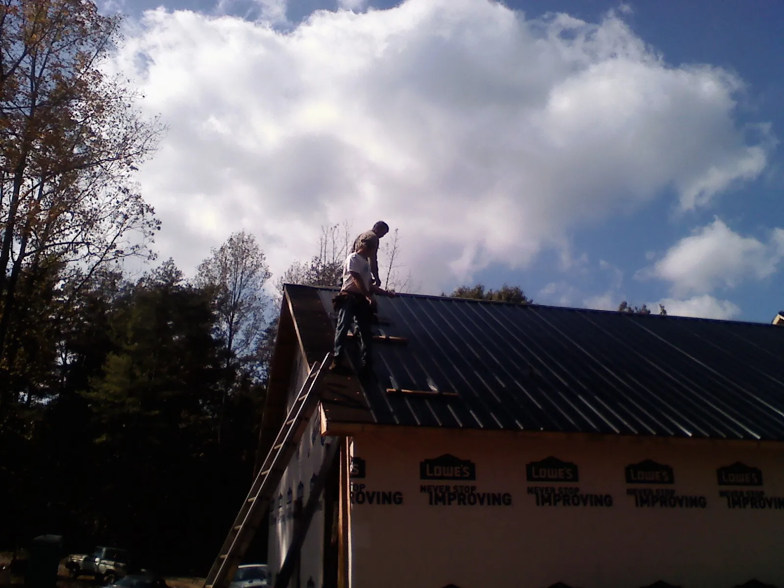 Roofer fastening dark metal panels high against a cloudy sky, from a Roof Inspection job in East Millsboro