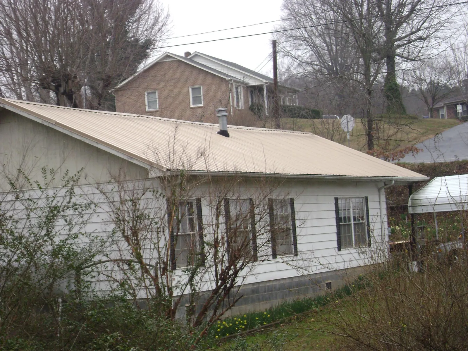 Tan metal roof on a white sided house set into a hillside — Commercial Roofing by Roofing Brothers in East Millsboro